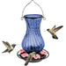 Blue glass hummingbird feeder with pink flowers and three hummingbirds on a white background