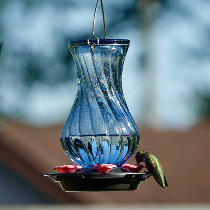 Blue glass hummingbird feeder with a blurred natural background