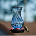 Blue glass hummingbird feeder with a blurred natural background