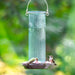 Decorative glass hummingbird feeder with two hummingbirds feeding on a blurred green background