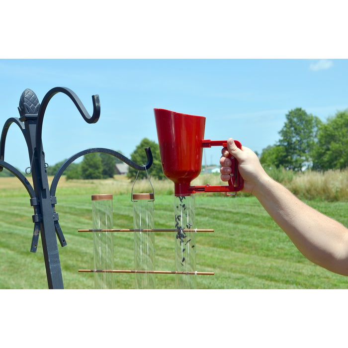 Person using a red funnel to fill bird feeders on a grassy outdoor setting