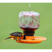 Orange bird feeder with a bird perched on it against a green background