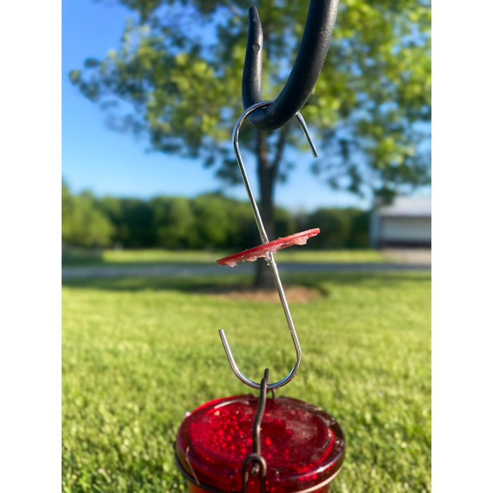 Red hummingbird feeder hanging from a hook with a blurred outdoor background