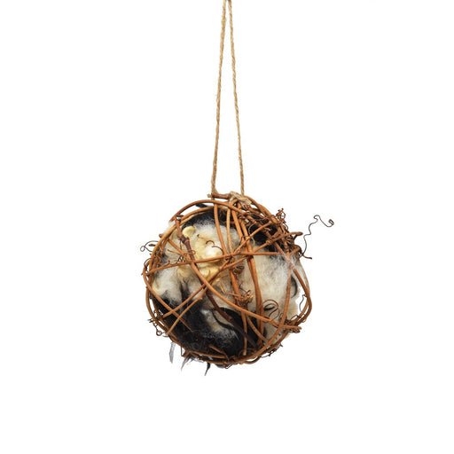 Decorative spherical object made of twigs with a small figurine inside, hanging on a white background.