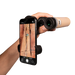 Hand holding a smartphone with a phone holder attached, displaying an image of a person climbing a rock wall. A telescope is pointed towards the screen.