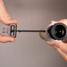 Two hands holding a camera lens and a lens cap against a gray background