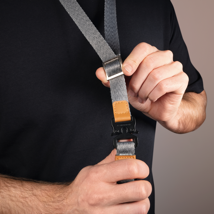 Person holding a gray strap with a buckle against a black background