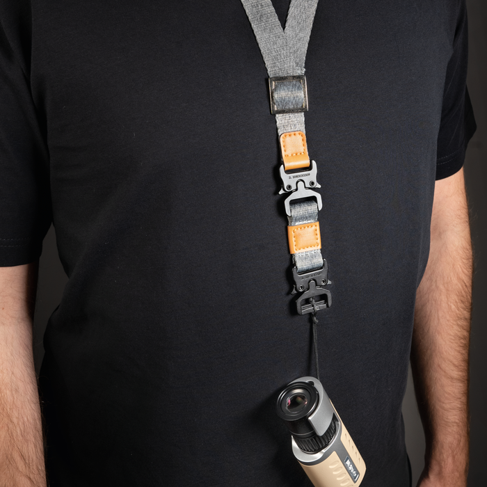 Person wearing a black shirt with a camera strap and lens attached, on a dark background