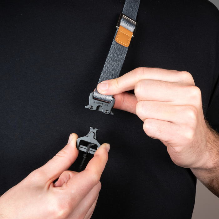 Person adjusting a gray strap with a buckle on a black background
