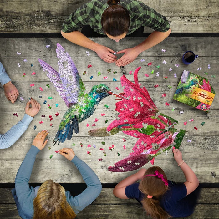 People working on a colorful puzzle of a hummingbird and flower on a wooden table.