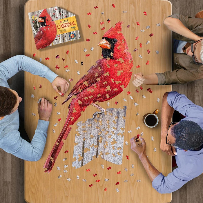 Two people working on a puzzle of a red cardinal bird at a wooden table.