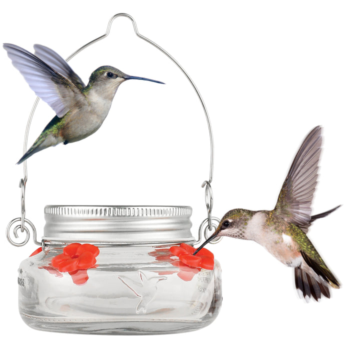 Glass hummingbird feeder with red flowers and two flying hummingbirds on a white background