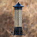 Bird feeder with bird seed and a small bird perched on it against a blurred natural background
