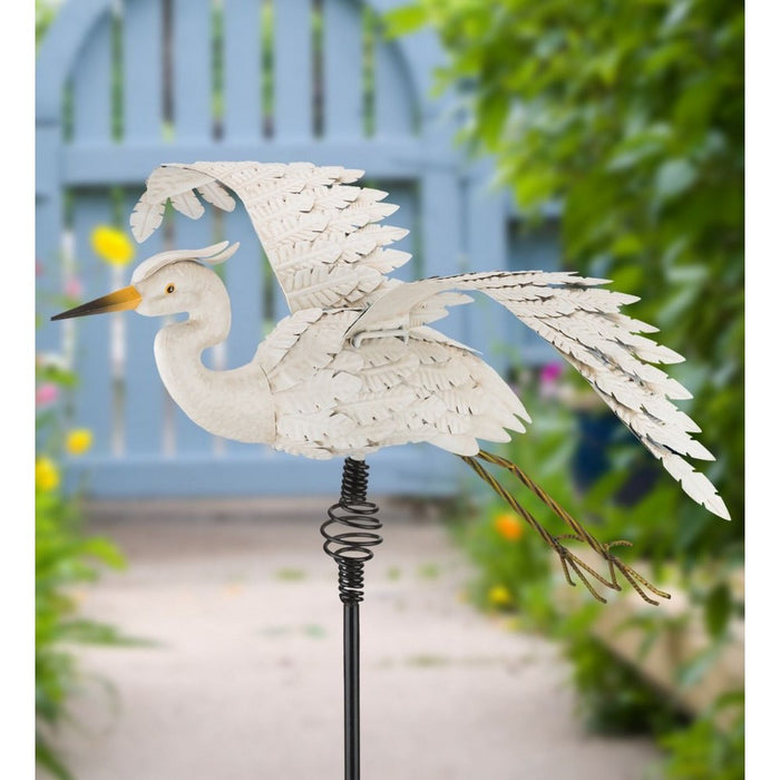 Decorative metal heron sculpture on a garden stake with a blurred garden background