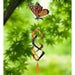 Butterfly-shaped wind chime with colorful spiral design against a green leafy background