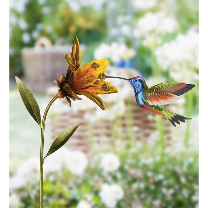 Decorative metal sculpture of a hummingbird and flower with a garden background