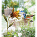 Decorative metal sculpture of a hummingbird and flower with a garden background