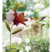 Decorative garden stake with a red flower and green hummingbird on a blurred garden background