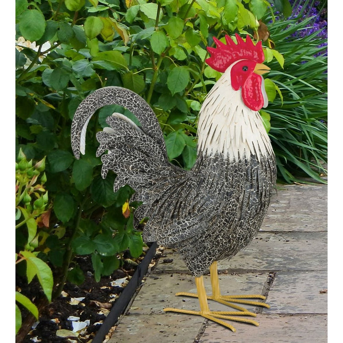 Decorative wire rooster sculpture on a wooden surface with greenery in the background