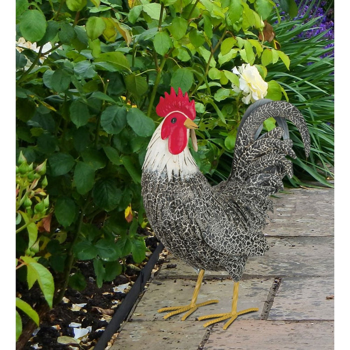 Decorative rooster on a wooden surface with greenery in the background