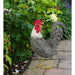 Decorative rooster on a wooden surface with greenery in the background