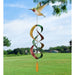 Colorful wind chime shaped like a hummingbird against a blue sky with trees and grass.