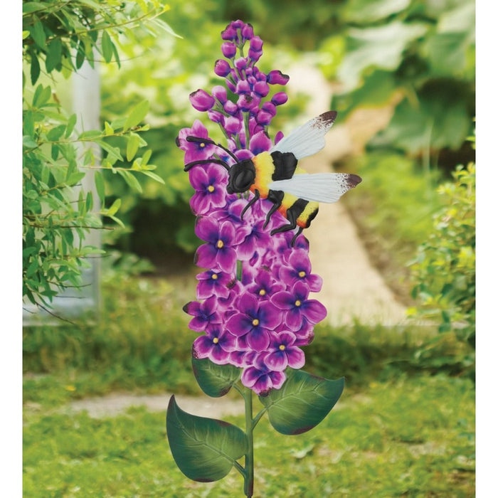 Decorative garden stake with purple flowers and a bee design, set against a natural outdoor background.