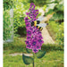 Decorative garden stake with purple flowers and a bee design, set against a natural outdoor background.
