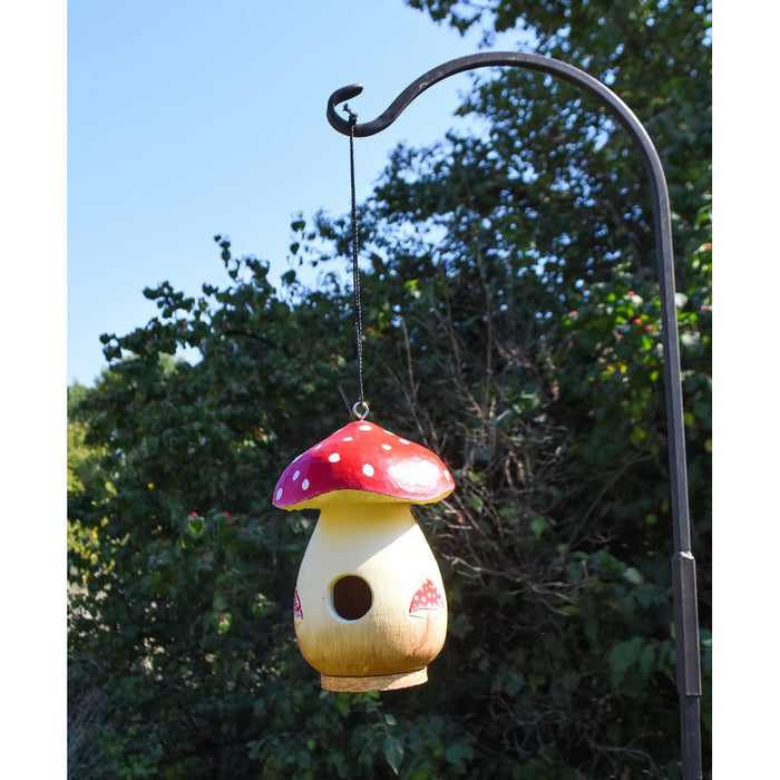 Mushroom-shaped birdhouse hanging from a hook against a natural background