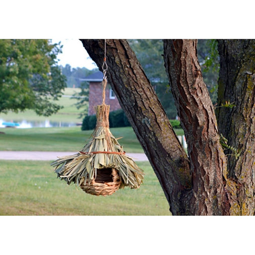 Handmade birdhouse made of natural materials hanging from a tree branch.