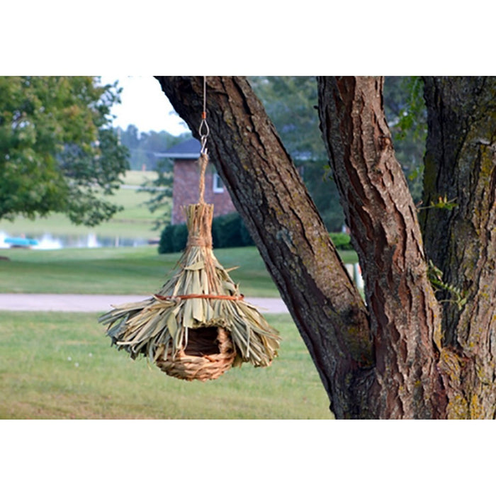 Handmade birdhouse made of natural materials hanging from a tree branch.