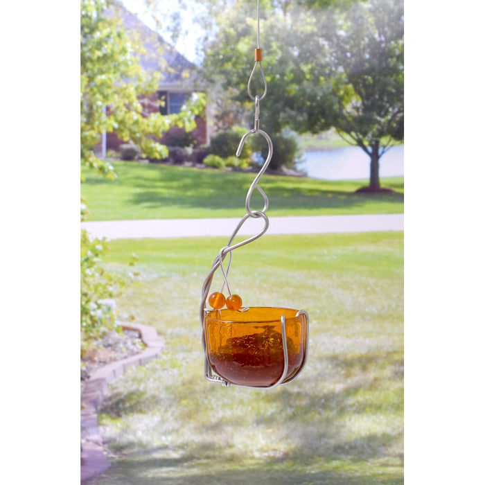 Glass bird feeder with orange berries hanging in a garden setting