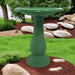 Green bird bath in a garden setting with rocks and grass.