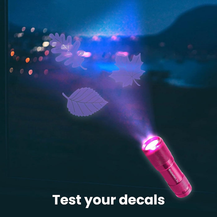 Pink flashlight projecting leaf-shaped decal onto a dark surface with colorful lights in the background.