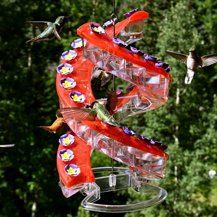 Hummingbird feeder with red and clear design, surrounded by hummingbirds against a green background